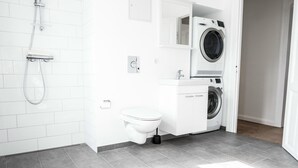 A modern bathroom with a shower, toilet, and stacked washing machines. - Beautiful 2-bed w Large Balcony (Copenhagen)