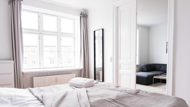Ein Hotelzimmer mit Bett, einem Vorhangfenster, einem Spiegel und Blick auf umliegende Gebäude.