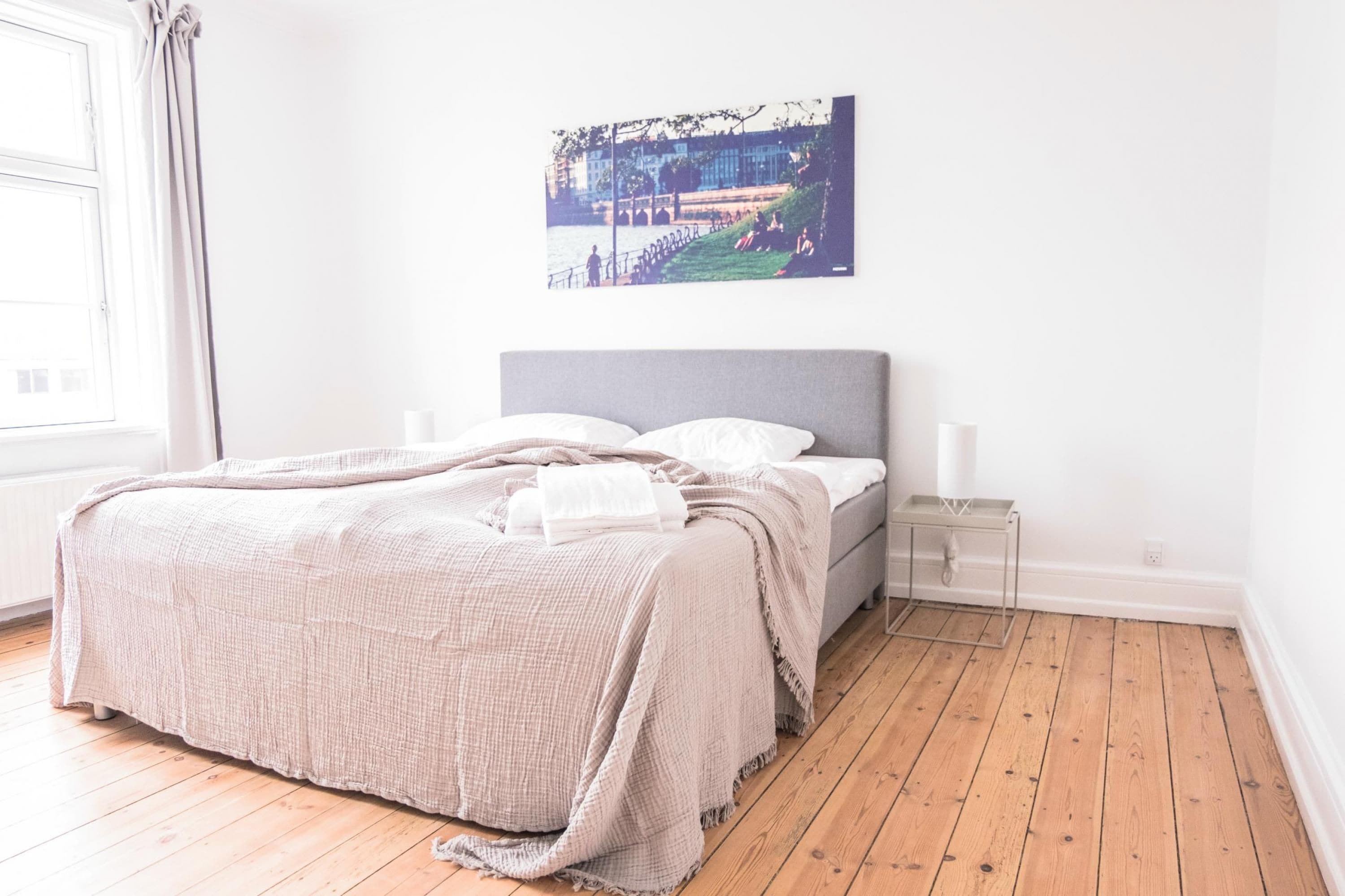 A bedroom with a bed, bedside tables, a window with curtains, and a wall-mounted picture.
