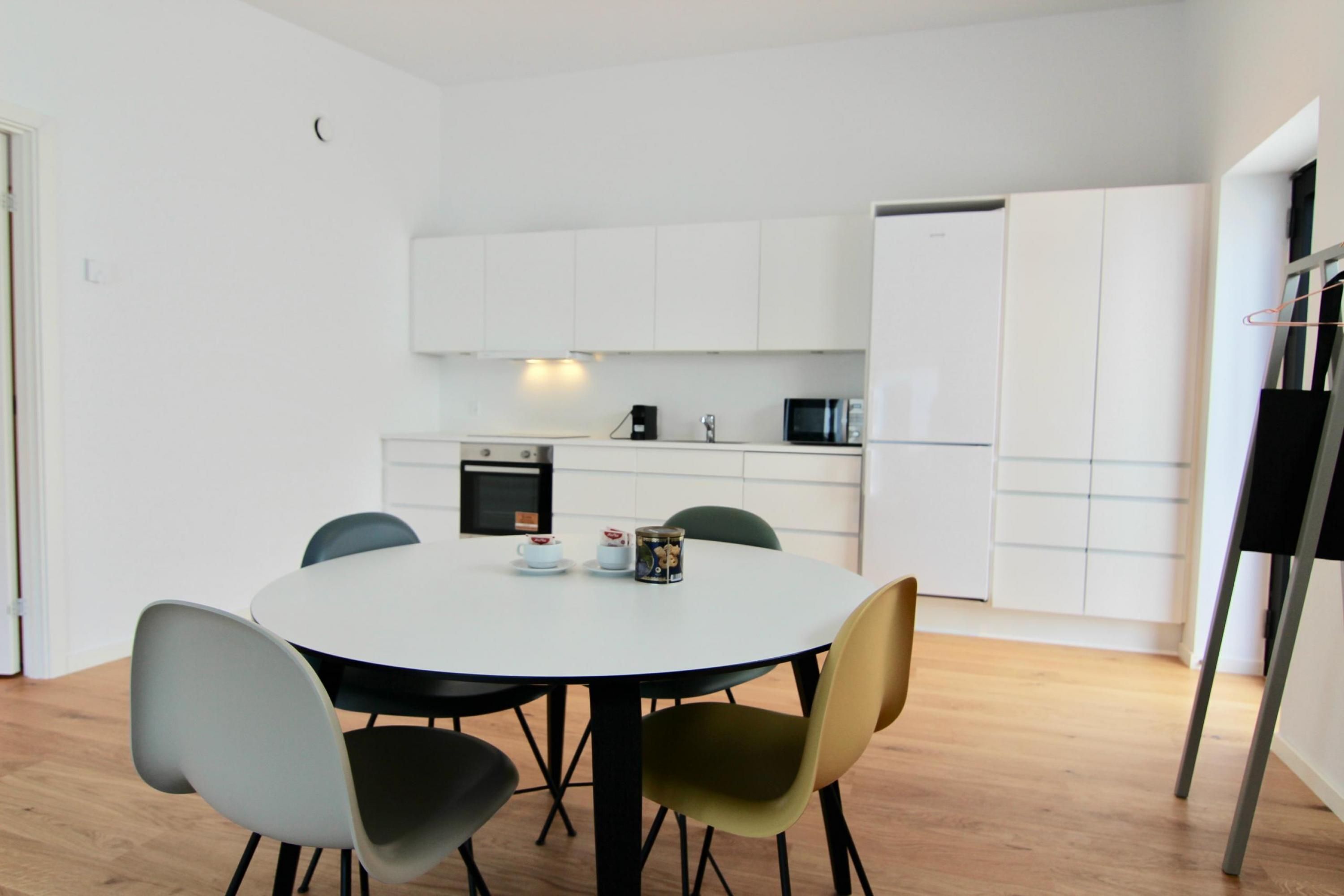 Een moderne keuken met witte kasten, een ronde eettafel met stoelen en een magnetron.