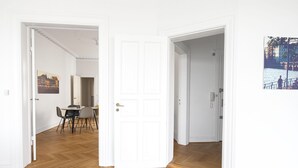 An open door leading to a dining area with a table and chairs, a white door with a gold handle, and a framed picture on the wall. - Fantastic 3-bed With French Balcony and Lake-views (Copenhagen)
