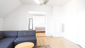 Egy modern, minimalista stílusú szoba, melyben sötétkék kanapé, egy fa kávézóasztal és egy fehér mennyezeti lámpatest található.