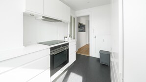 Egy modern konyha fehér szekrényekkel, fekete tűzhellyel és szürke színű szemetesedénnyel.