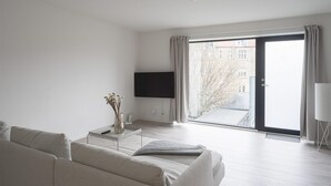 Un salon moderne avec un canapé, un téléviseur à écran plat et une porte-fenêtre coulissante donnant sur un espace extérieur.