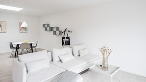 Un salon moderne avec un canapé blanc, une table à manger avec des chaises, une suspension et un élément décoratif mural.