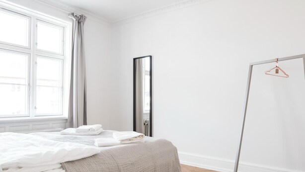 A bedroom with a bed, a wardrobe, a mirror, and a window with curtains. - Beautiful 2-bed With Large Balcony (Copenhagen)