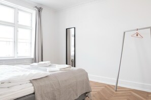 A bedroom with a bed, a wardrobe, a mirror, and a window with curtains. - Beautiful 2-bed With Large Balcony (Copenhagen)
