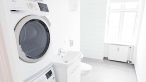 Une buanderie moderne équipée d’un lave-linge et d’un sèche-linge à chargement frontal, d’un évier et de toilettes.