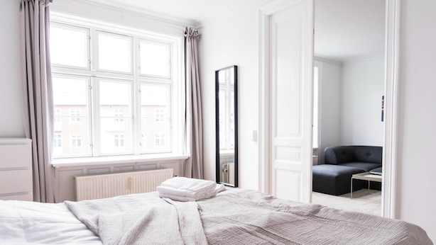 Une chambre d’hôtel avec un lit, une fenêtre avec des rideaux, un miroir et une vue sur les bâtiments environnants.