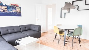 Un salon moderne avec un canapé gris, une table basse blanche et un coin repas comprenant une table ronde et des chaises colorées.