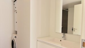 Un baño pequeño con lavadora, lavamanos y espejo, y una puerta.