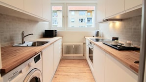 A compact kitchen with a washing machine, a coffee maker, and a window with a view of a building. - Lovely 2-bed in Frederiksberg w Balcony - 177 (Frederiksberg)