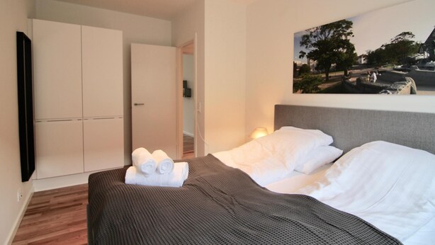 A hotel room with a bed, a wardrobe, a painting on the wall, and a door leading to another room. - Lovely 2-bed in Frederiksberg w Balcony - 177 (Frederiksberg)