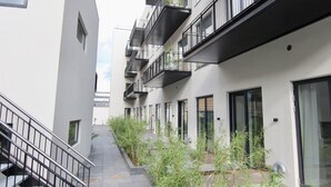 Ein modernes Mehrfamilienhaus mit Balkonen, einer zentralen Treppe und einem mit Pflanzen bepflanzten Weg.