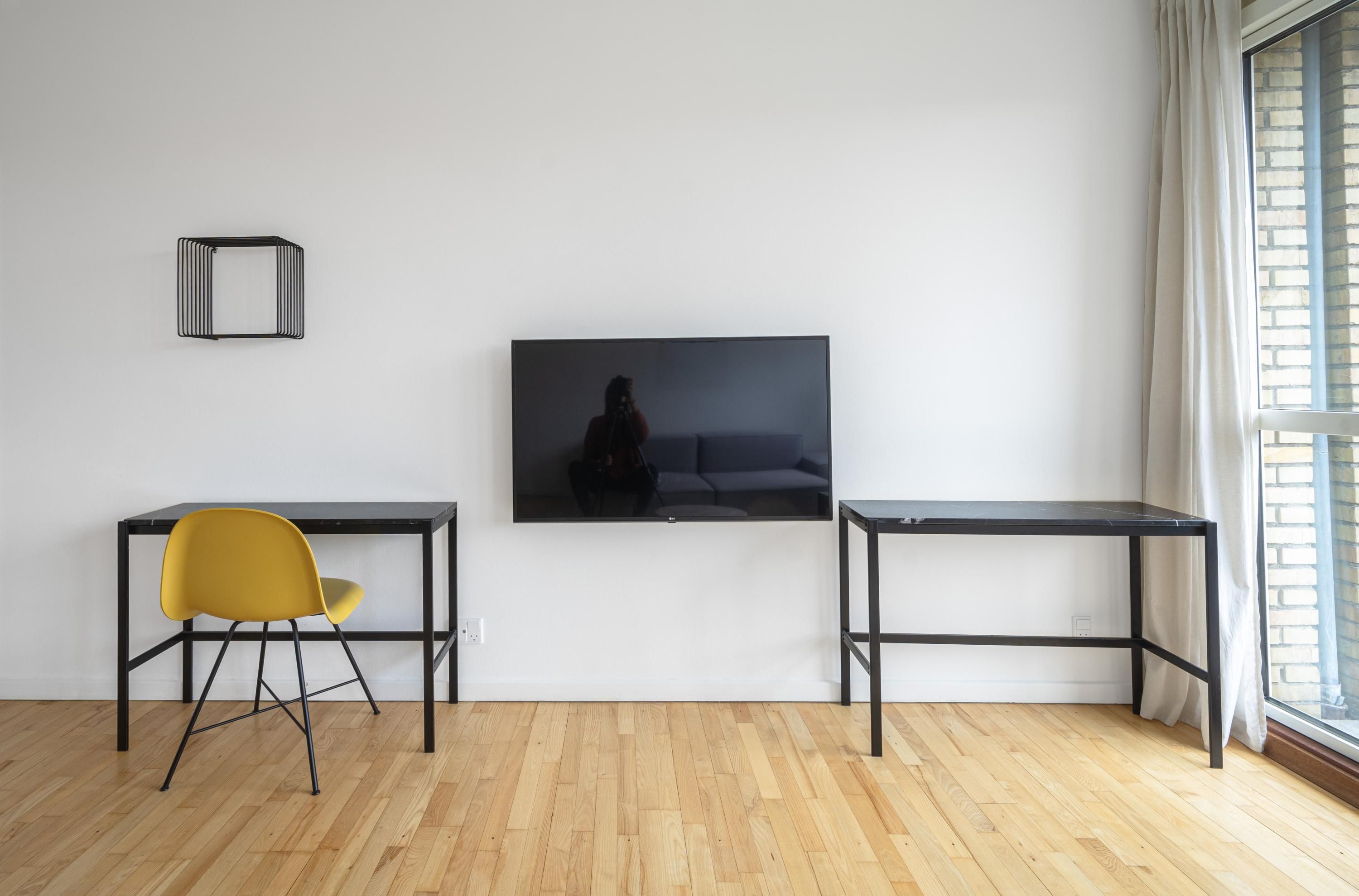 Ein modernes Wohnzimmer mit einem wandmontierten Flachbildfernseher, einem gelben Sessel und zwei schwarzen Tischen.