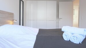A hotel room with a bed, a wardrobe, and a rolled towel on the bed. - Great 2-bed w Balcony (Frederiksberg)