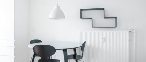 Un espace de salle à manger moderne avec une table blanche, des chaises noires, un luminaire suspendu blanc et un élément décoratif géométrique sur le mur.