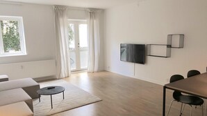 Ein großzügiger Wohnbereich mit Sofa, Couchtisch, Wandfernseher und Esstisch mit Stühlen.