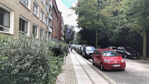 Eine Straße mit geparkten Autos, im Vordergrund ein rotes Auto.