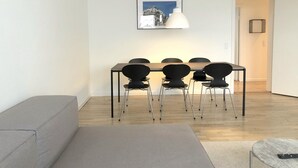 A modern living room with a dining table, four chairs, a grey sofa, and a small round table with a remote control. - Nice 2-bed in Frederiksberg (Frederiksberg)