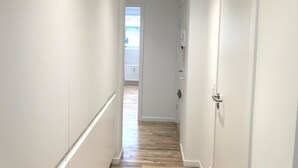 A narrow hallway with white walls and wooden flooring leading to a door. - Nice 2-bed in Frederiksberg (Frederiksberg)