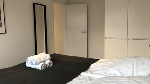 A hotel room with a bed, a black textured bedspread, a white blanket with rolled towels, a large mirror, and a wardrobe with a door. - Nice 2-bed in Frederiksberg (Frederiksberg)