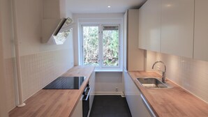 A modern kitchen with white cabinets, a black countertop, a stainless steel sink, and a window with a view of trees. - Great 2-bed w Balcony in Charlottenlund (Charlottenlund)