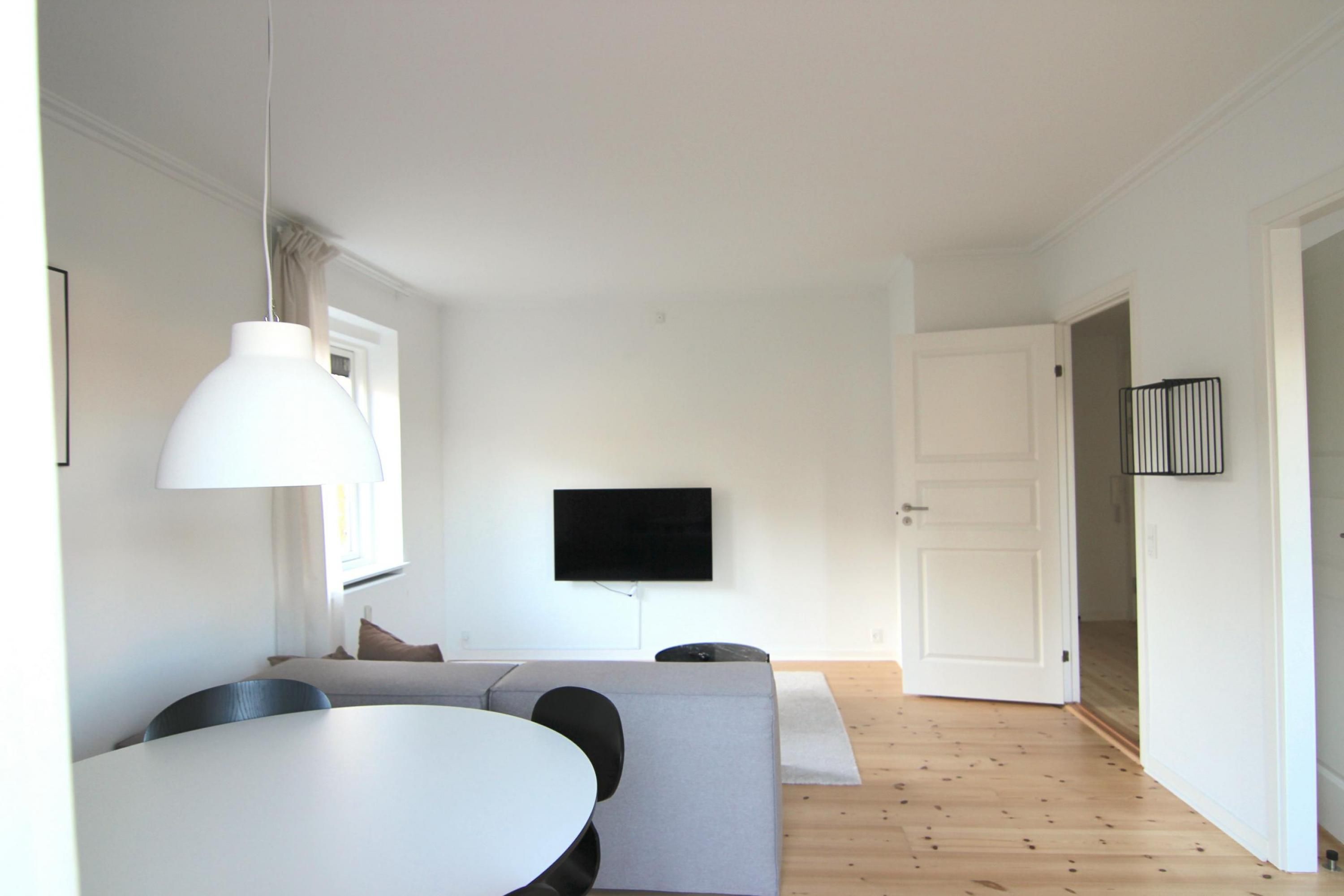Ein modernes Wohnzimmer mit Esstisch, Sofa und einem flachbildfernseher an der Wand.