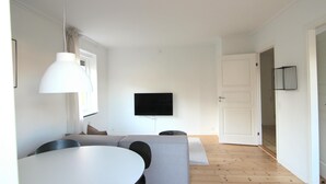 A modern living room with a dining table, sofa, and a flat-screen TV mounted on the wall. - Great 2-bed w Balcony in Charlottenlund (Charlottenlund)