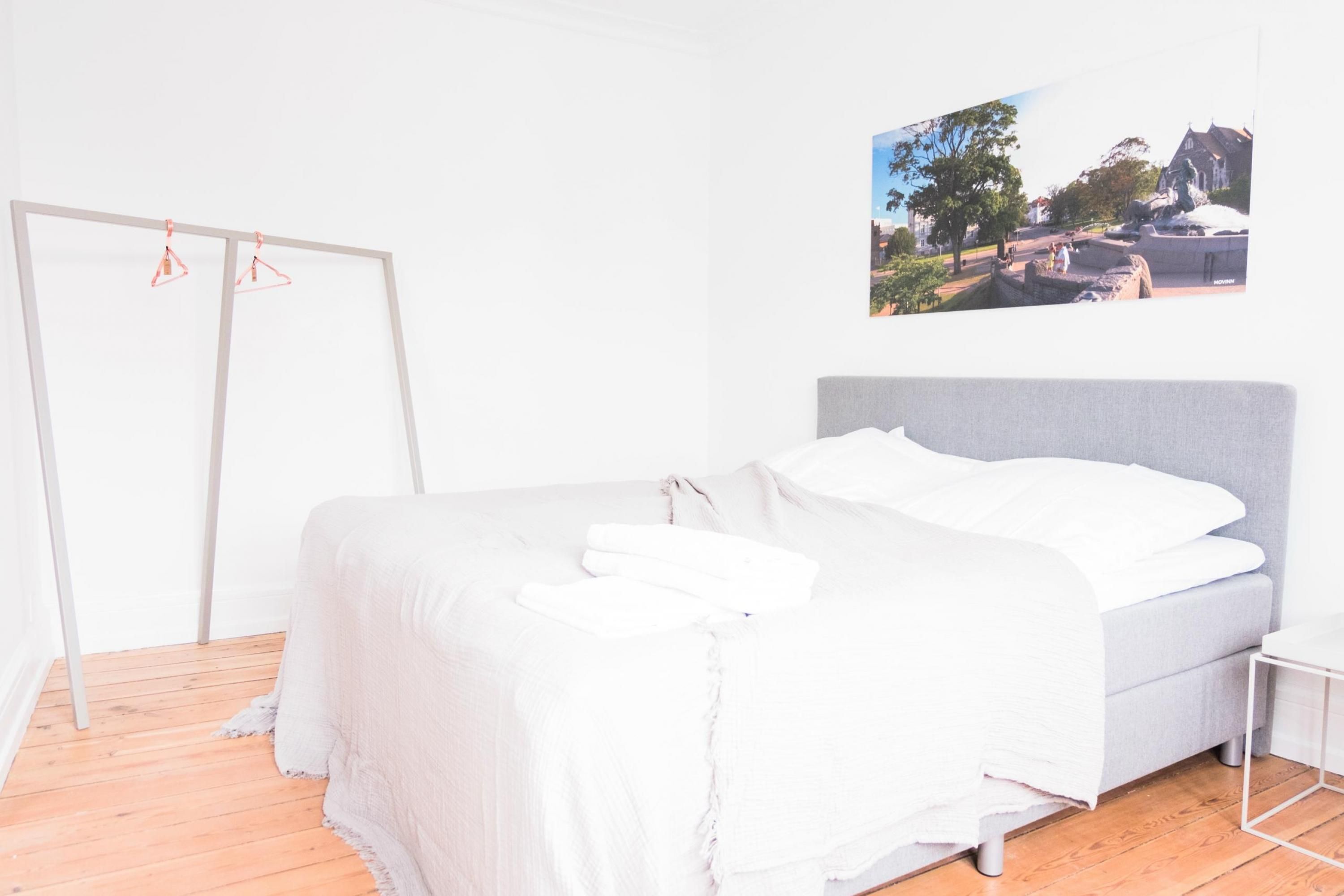 A bedroom with a bed, a wooden floor, a white wardrobe, and a wall-mounted picture.