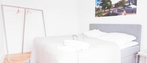 A bedroom with a bed, a wooden floor, a white wardrobe, and a wall-mounted picture.