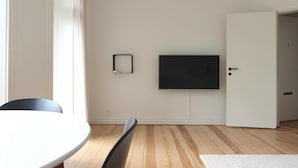 Une pièce avec une table de salle à manger ronde, une chaise noire, un téléviseur à écran plat fixé au mur et une porte blanche.