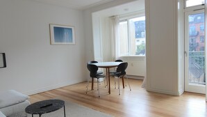 Un salon spacieux avec un canapé blanc, une petite table basse noire et un coin repas comprenant une table blanche et quatre chaises noires.