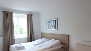 Un lit bien fait, avec du linge de lit blanc, une tête de lit en bois et une fenêtre avec des rideaux.