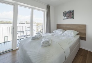 Une chambre d’hôtel avec un grand lit, un balcon avec une chaise et une vue sur la ville.