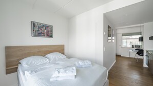 A modern hotel room with a large bed, a desk, and a view of the cityscape through the window.