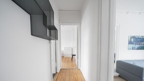 Un couloir avec un plancher en bois, des murs blancs et un canapé gris à l’arrière-plan.