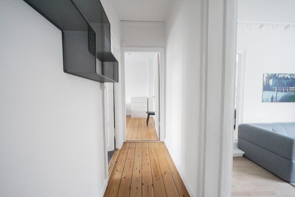 A hallway with wooden flooring, white walls, and a gray sofa in the background.