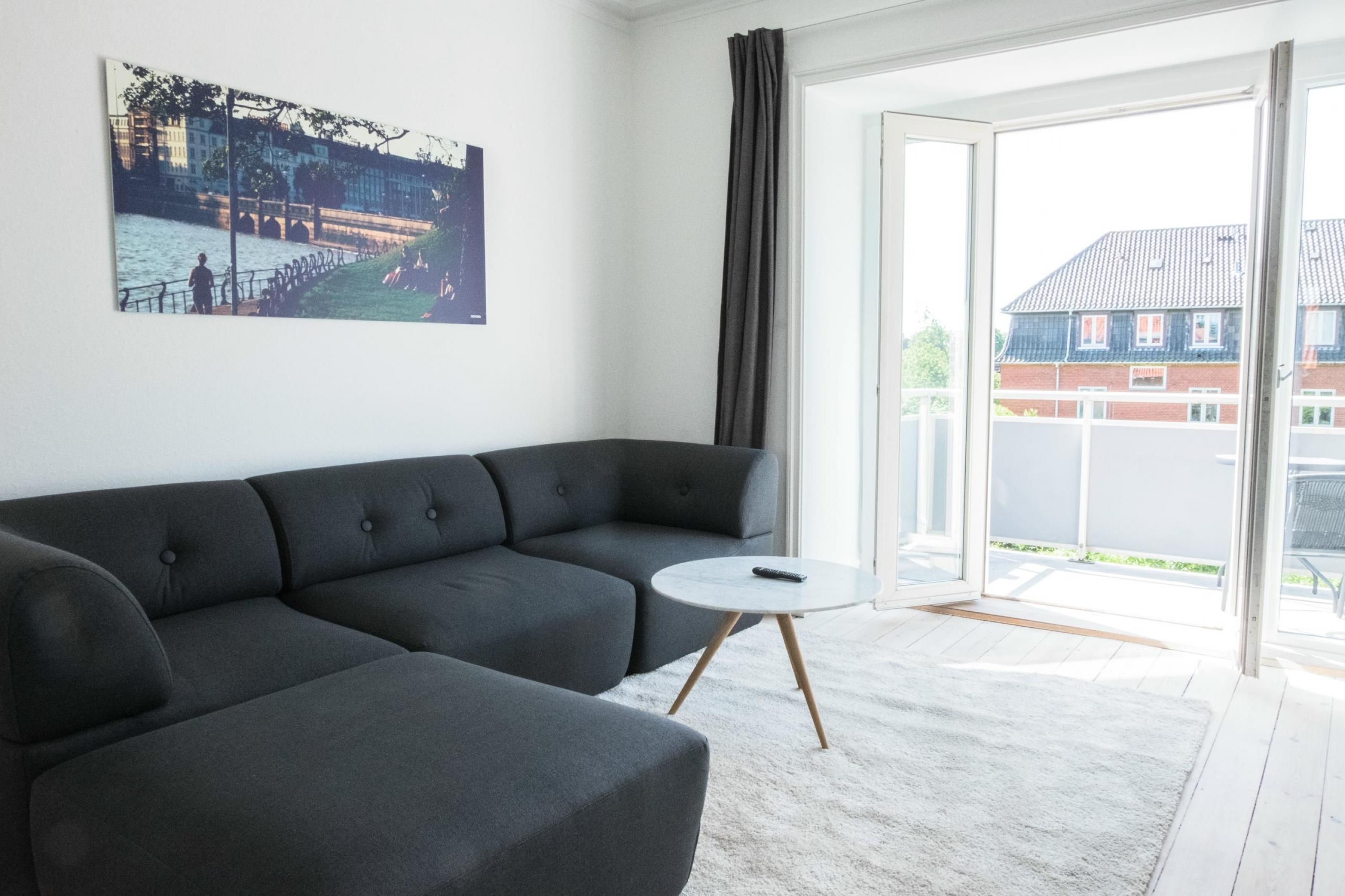 A modern living room with a sectional sofa, a small round table, and a large window with a view of a building and a bridge.