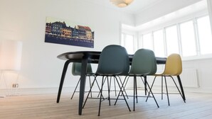 Een moderne eetruimte met een ronde tafel, vier stoelen, een stadsgezicht schilderij en een bijzondere plafondlamp.