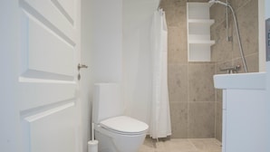 Un baño con inodoro, ducha y paredes de azulejos blancos.