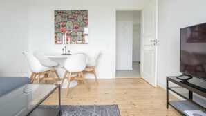 Una sala de estar moderna con un televisor, una mesa de comedor con sillas y una obra de arte colorida en la pared.