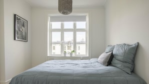 Un dormitorio con un ventanal grande, una cama con ropa de cama gris y una lámpara colgante.
