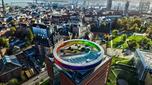 A modern building with a circular glass atrium, surrounded by a mix of older and newer architecture, with a view of a river and industrial structures in the background. - 2-bed Apartment in one of Rhus Best Locations (Aarhus)