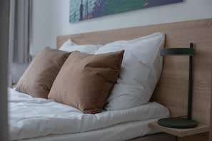 A neatly made bed with white and brown pillows, a wooden headboard, and a bedside table with a modern lamp. - Beautiful 2-bed in top Location (Copenhagen)