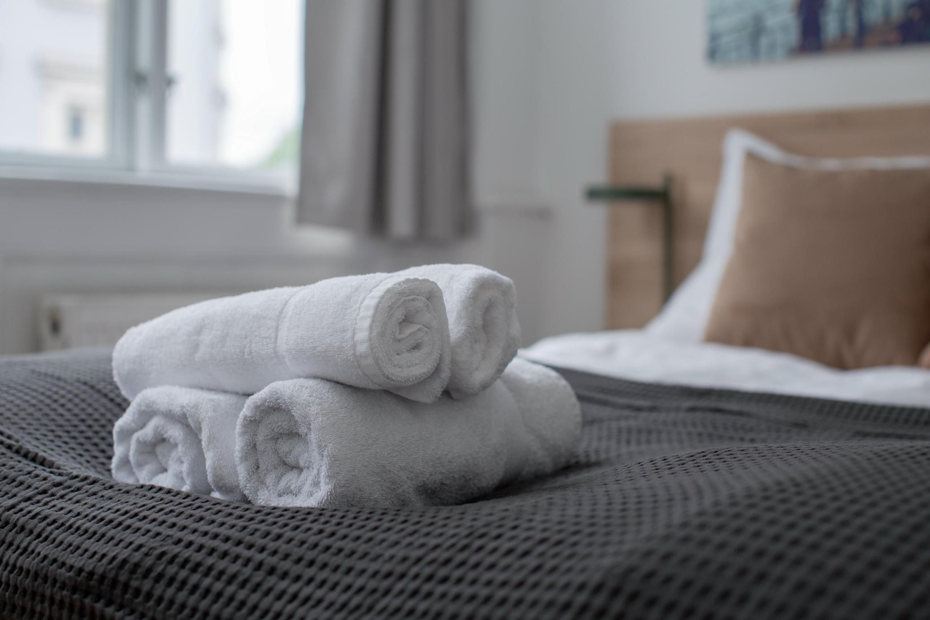 Una cama bien hecha con toallas blancas enrolladas y una colcha gris con textura.