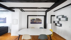 Ein moderner Konferenzraum mit einem weißen Tisch, vier Stühlen, einem Stadtbildgemälde und schwarzer geometrischer Wandgestaltung.