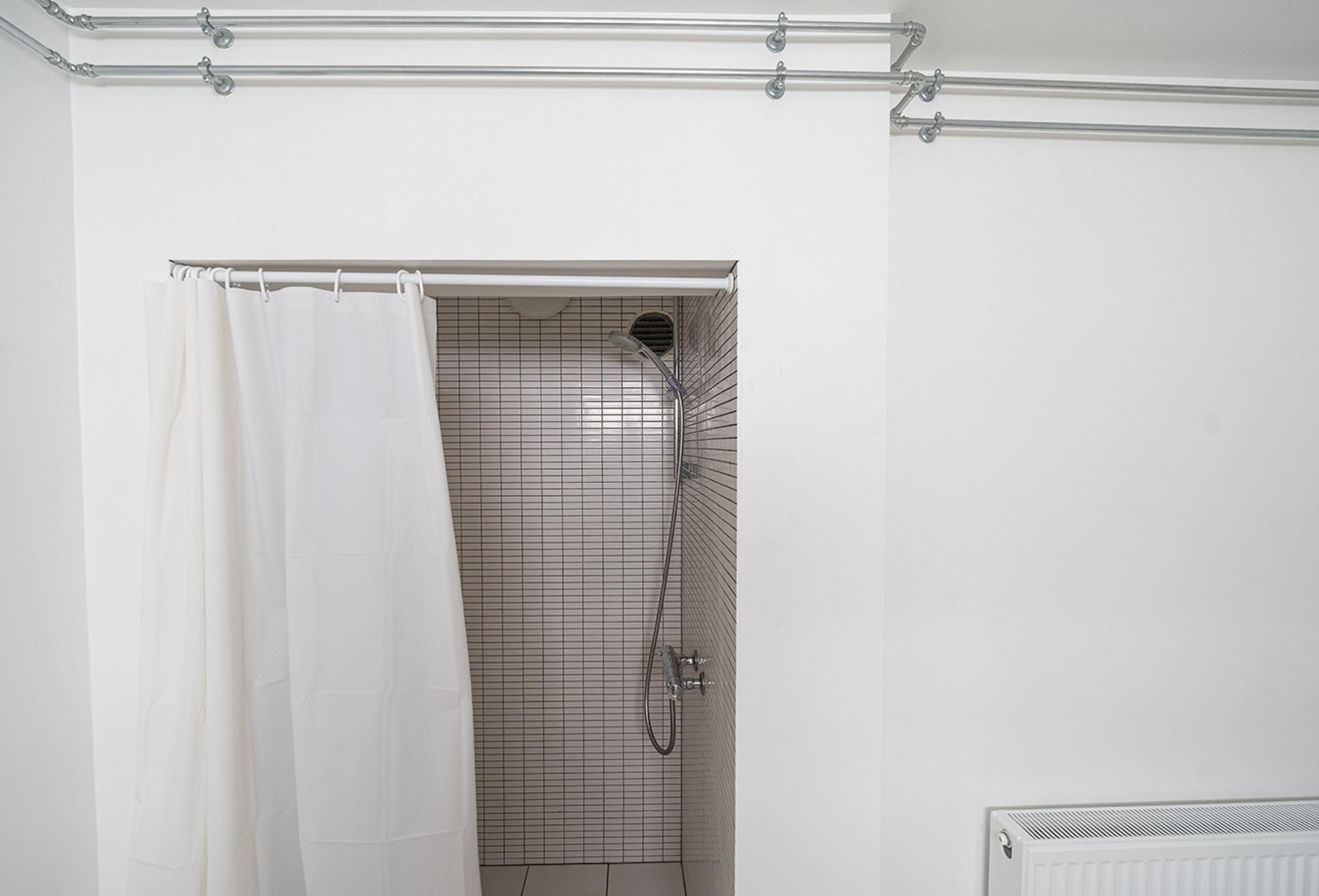 Un espace douche avec un rideau blanc, un mur carrelé et une pomme de douche en métal.
