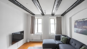 Ein modernes Wohnzimmer mit grauem Sofa, einem Flachbildfernseher an der Wand und einem großen Fenster mit Vorhängen.