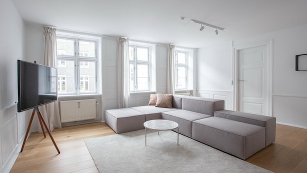 A modern living room with a sectional sofa, a small round table, and a flat-screen TV on a tripod stand. - Beautiful 2-bed in top Copenhagen Location (Copenhagen)